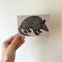 Load image into Gallery viewer, Armadillo linocut art printed on brown chipboard postcard.